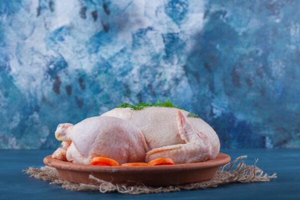 Whole chicken and sliced carrots on a plate on a burlap napkin, on the blue background. High quality photo